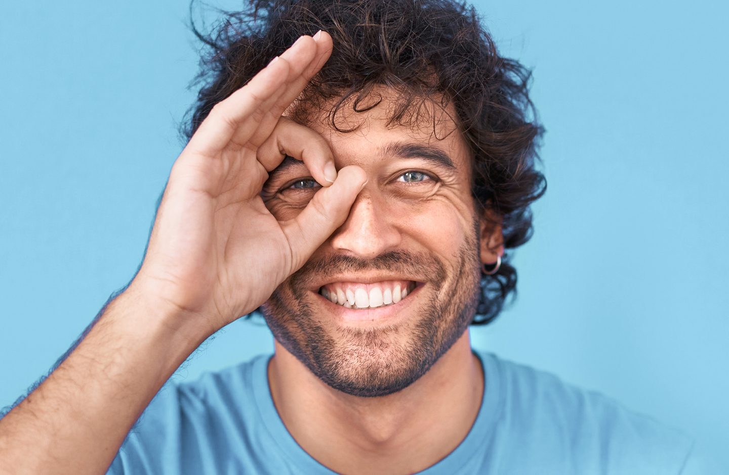 Ein Mann formt mit seinen Fingern einen Kreis und hält ihn lachend vor sein Auge.